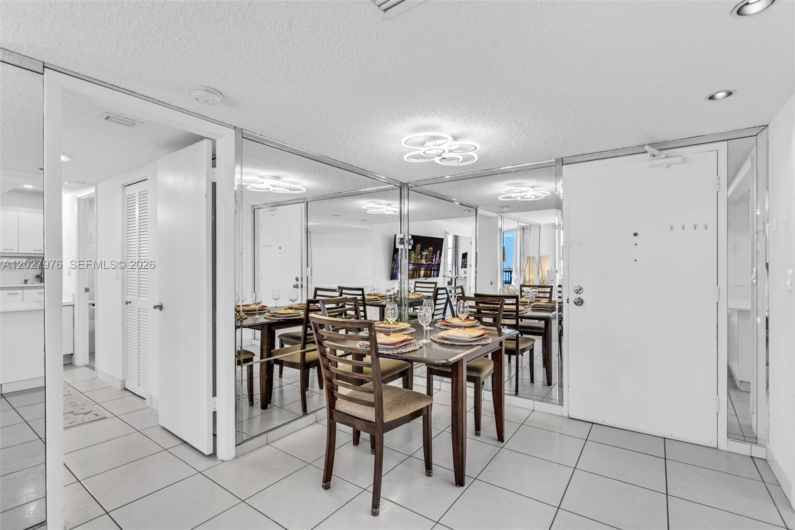 A dining area features a wooden table, chairs, tiled floors, and a mirrored wall — 9273 Collins Ave # 503, Surfside FL 33154, SURFSIDE, FL