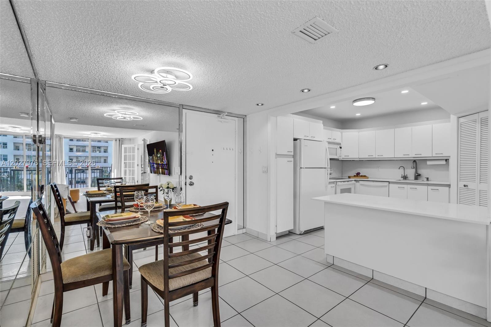 A dining area with a wooden table and chairs sits adjacent to a white kitchen — 9273 Collins Ave # 503, Surfside FL 33154, SURFSIDE, FL