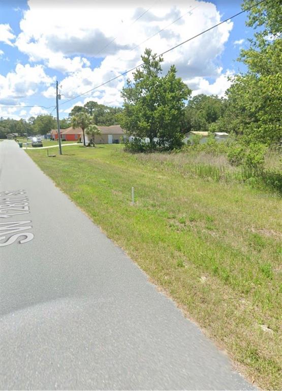 A grassy, undeveloped residential lot sits alongside a paved street with utility lines overhead — SW 128 STREET, OCALA, FL