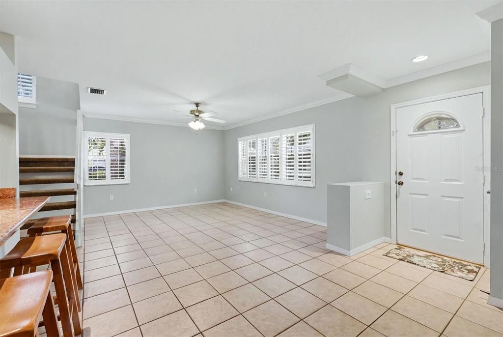 An open living area features light-colored tile flooring, white walls, plantation shutters, and a staircase — 2310 64TH STREET COURT W, BRADENTON, FL