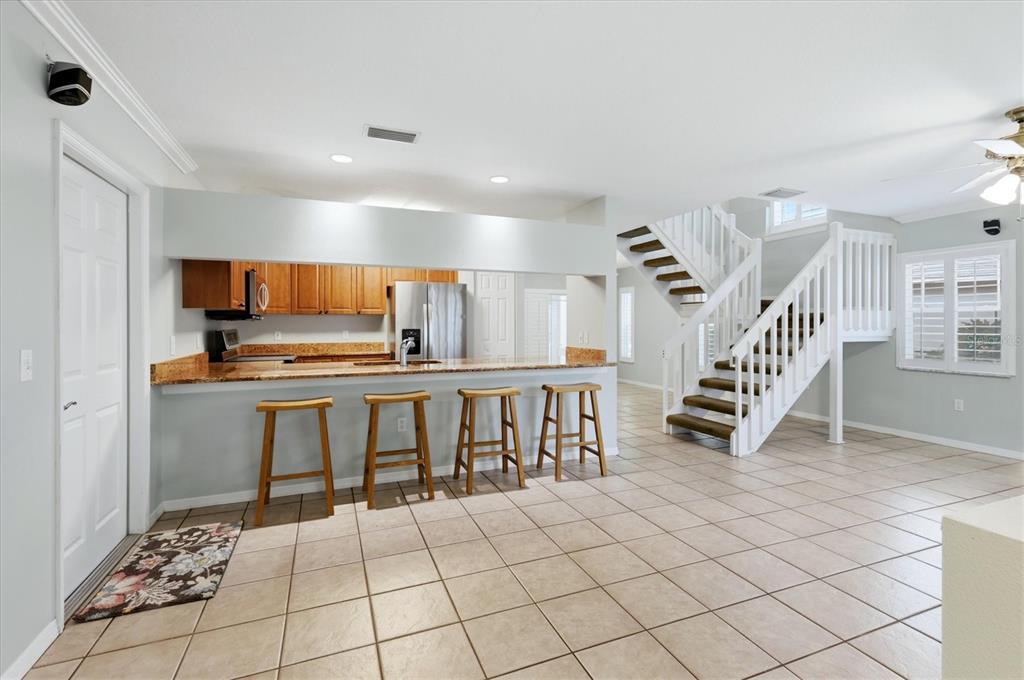 A kitchen with a breakfast bar and wooden stools sits next to a white staircase — 2310 64TH STREET COURT W, BRADENTON, FL