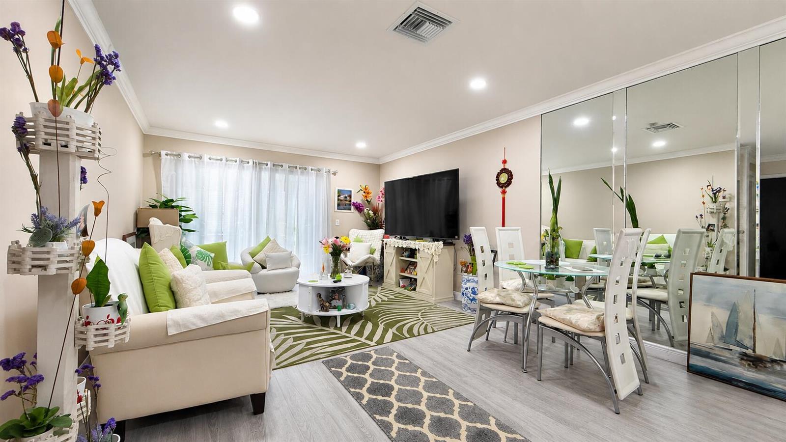 A living and dining area with light wood floors, a television, and mirrored wall panels — 2716 E Emory Dr Drive E # D, West Palm Beach FL 33415, WEST PALM BEACH, FL