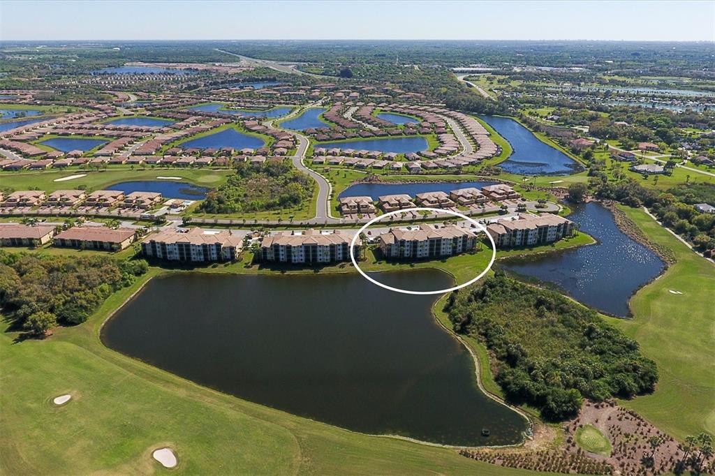 An aerial view shows a multi-story apartment building circled next to a large pond — 6509 GRAND ESTUARY TRAIL UNIT 108, BRADENTON, FL
