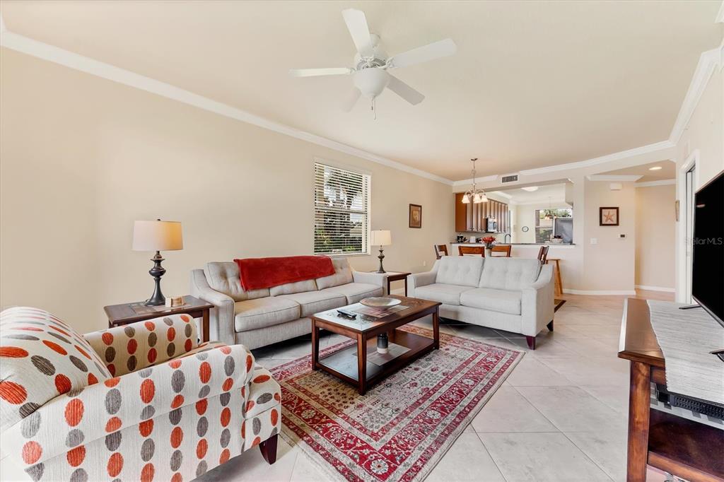 A living room features light-colored sofas, a patterned armchair, and a coffee table on tile — 6509 GRAND ESTUARY TRAIL UNIT 108, BRADENTON, FL