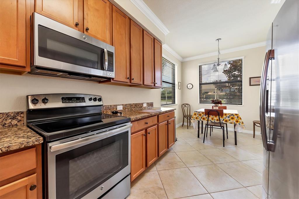 A kitchen with wood cabinets, granite countertops, stainless steel appliances, and an adjacent dining area — 6509 GRAND ESTUARY TRAIL UNIT 108, BRADENTON, FL