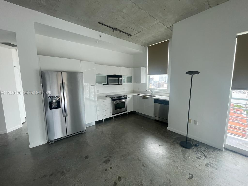 A modern kitchen features white cabinetry, stainless steel appliances, and polished concrete floors — 133 NE 2 AVE # 1813, Miami FL 33132, MIAMI, FL