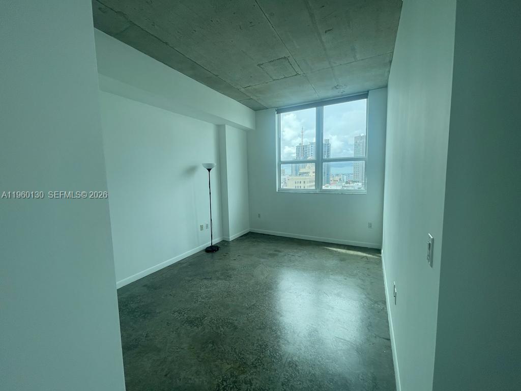 An empty room features polished concrete floors, white walls, and a large window with city views — 133 NE 2 AVE # 1813, Miami FL 33132, MIAMI, FL