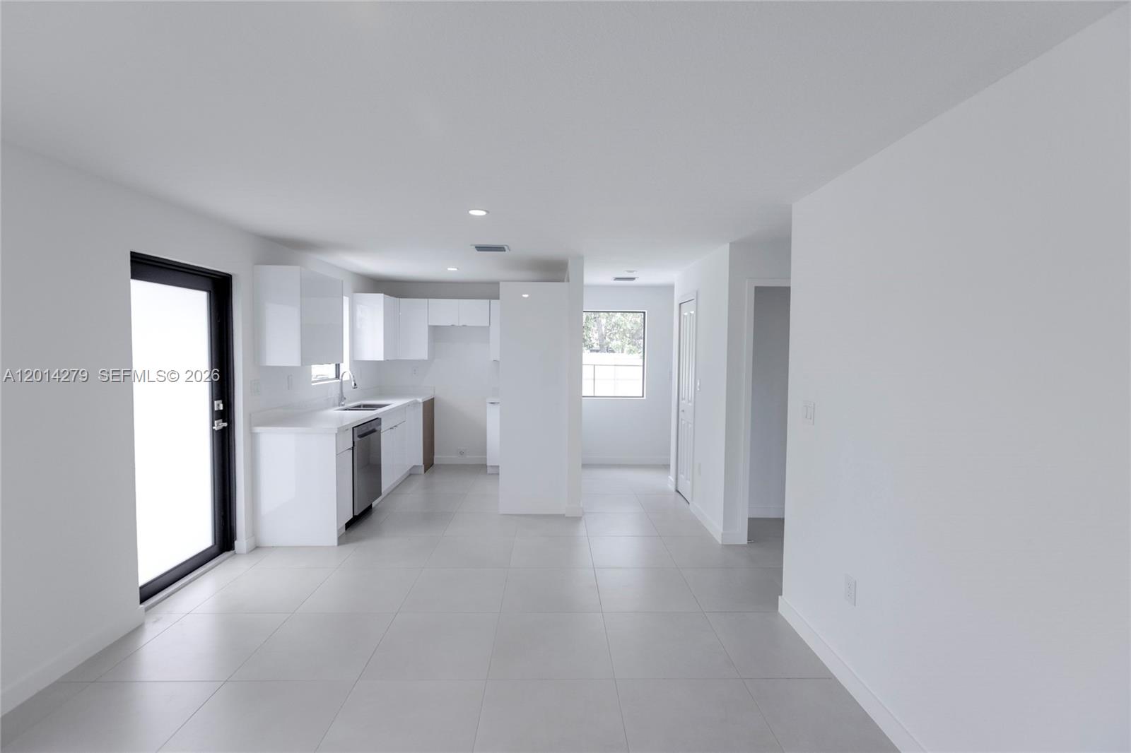 A modern, minimalist kitchen features white cabinetry, stainless steel appliances, and light-colored tile flooring — 9151 NW 32 Ave, Miami FL 33147, MIAMI, FL