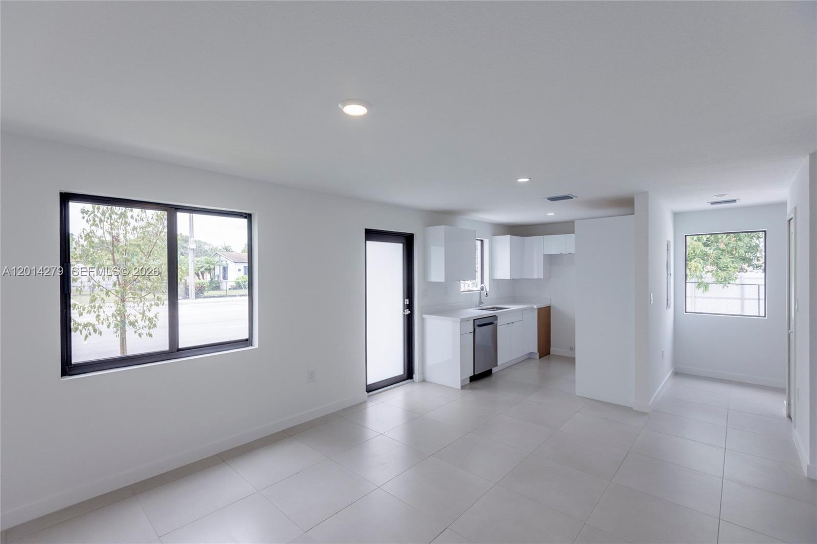 A bright, minimalist kitchen and living area features white cabinets, tile floors, and large windows — 9151 NW 32 Ave, Miami FL 33147, MIAMI, FL