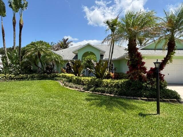 A light green house with a tiled roof is surrounded by palm trees and landscaping — 246 SE Ashley Oaks Way, Stuart FL 34997, STUART, FL