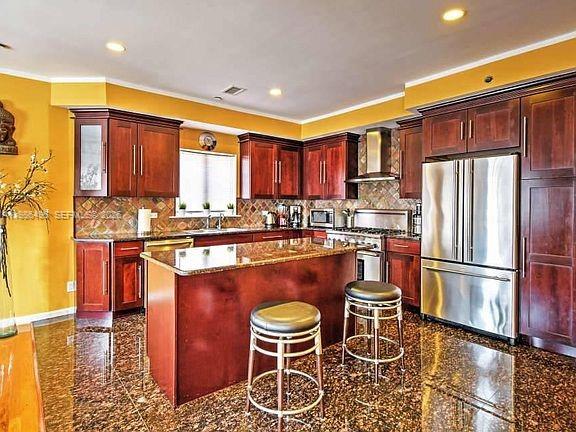 A kitchen features dark wood cabinets, a granite island with two stools, and stainless appliances — 2841 Ford # 2, NY 11235, NY