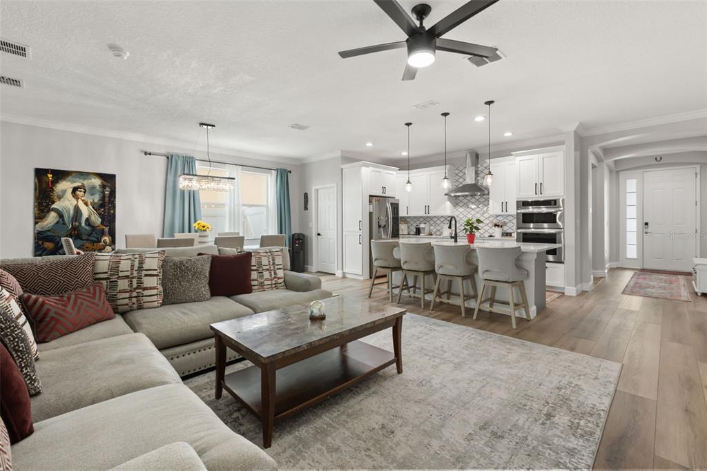 An open-concept living room and kitchen featuring light wood floors, white cabinetry, and a sectional — 268 JYOTI DRIVE, DAVENPORT, FL