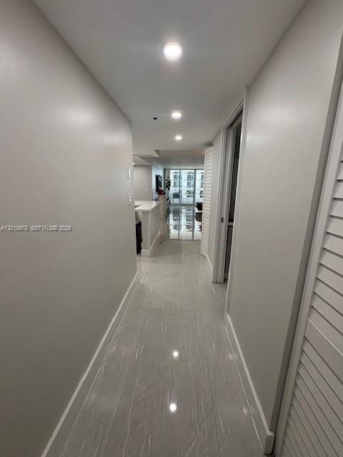 A hallway with light-colored walls and glossy tile flooring leads toward a bright living area — 1717 N Bayshore Dr # 1542, Miami FL 33132, MIAMI, FL