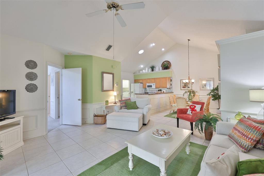 A living room with vaulted ceilings, tile floors, and an open kitchen in the background — 1115 GOLFVIEW WOODS DRIVE, SUN CITY CENTER, FL