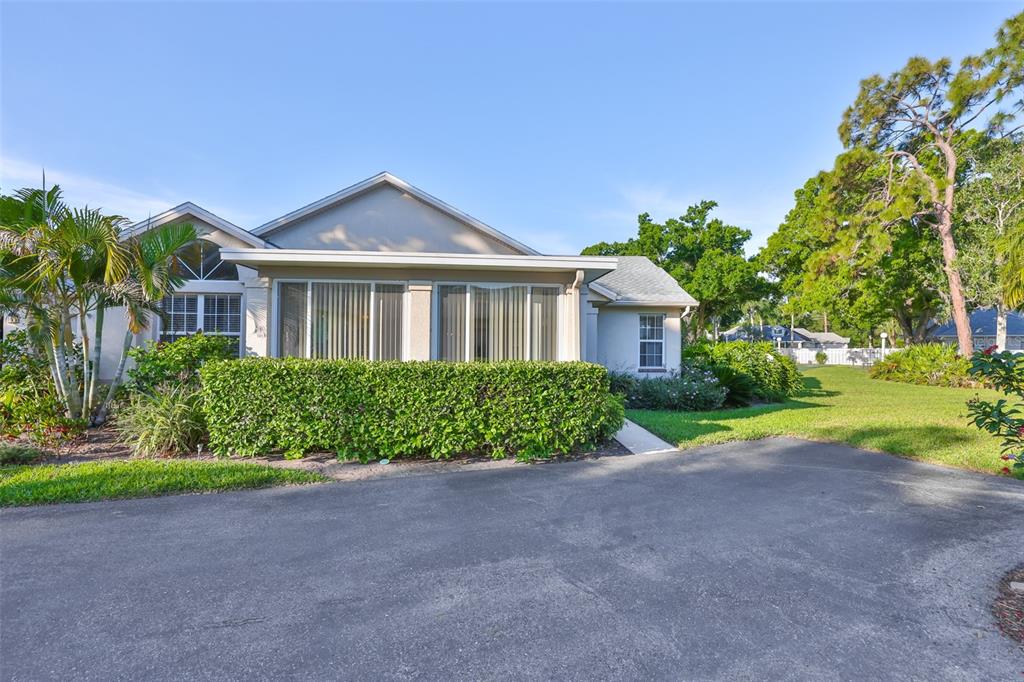 A single-story house with a paved driveway, a large hedge, and a sunroom exterior — 1115 GOLFVIEW WOODS DRIVE, SUN CITY CENTER, FL