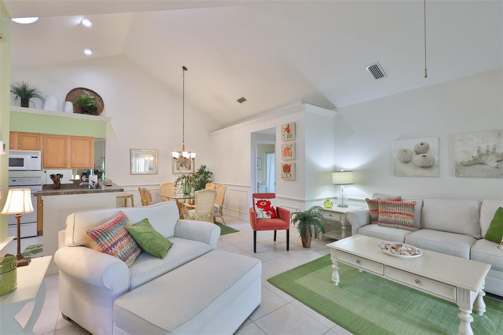 A living room and dining area with vaulted ceilings, light tile floors, and neutral furniture — 1115 GOLFVIEW WOODS DRIVE, SUN CITY CENTER, FL