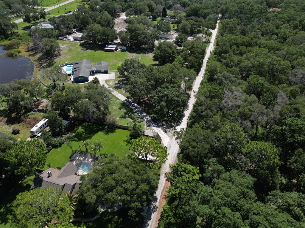 An aerial view shows two houses with swimming pools surrounded by trees and a dirt road — 1313 RED PONY RANCH ROAD, DELAND, FL