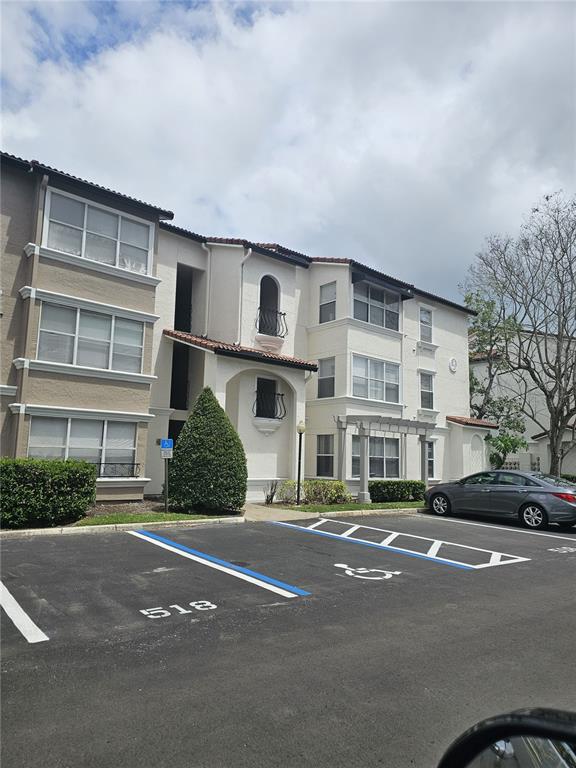 A three-story apartment building features beige stucco walls, a tiled roof, and a parking lot — 5132 CONROY ROAD UNIT 932, ORLANDO, FL