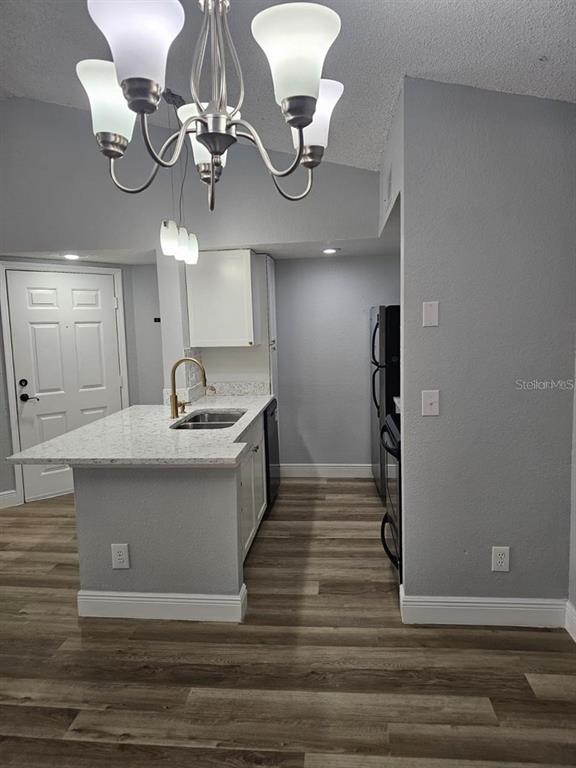 A kitchen features a granite-topped island with a sink, white cabinetry, and wood-look flooring — 5132 CONROY ROAD UNIT 932, ORLANDO, FL