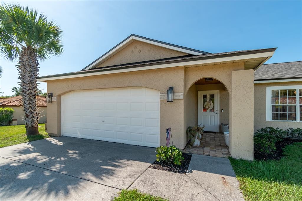 A tan stucco house features a white garage door, a covered entryway, and a palm tree — 308 OAK LANE PASS, OCALA, FL