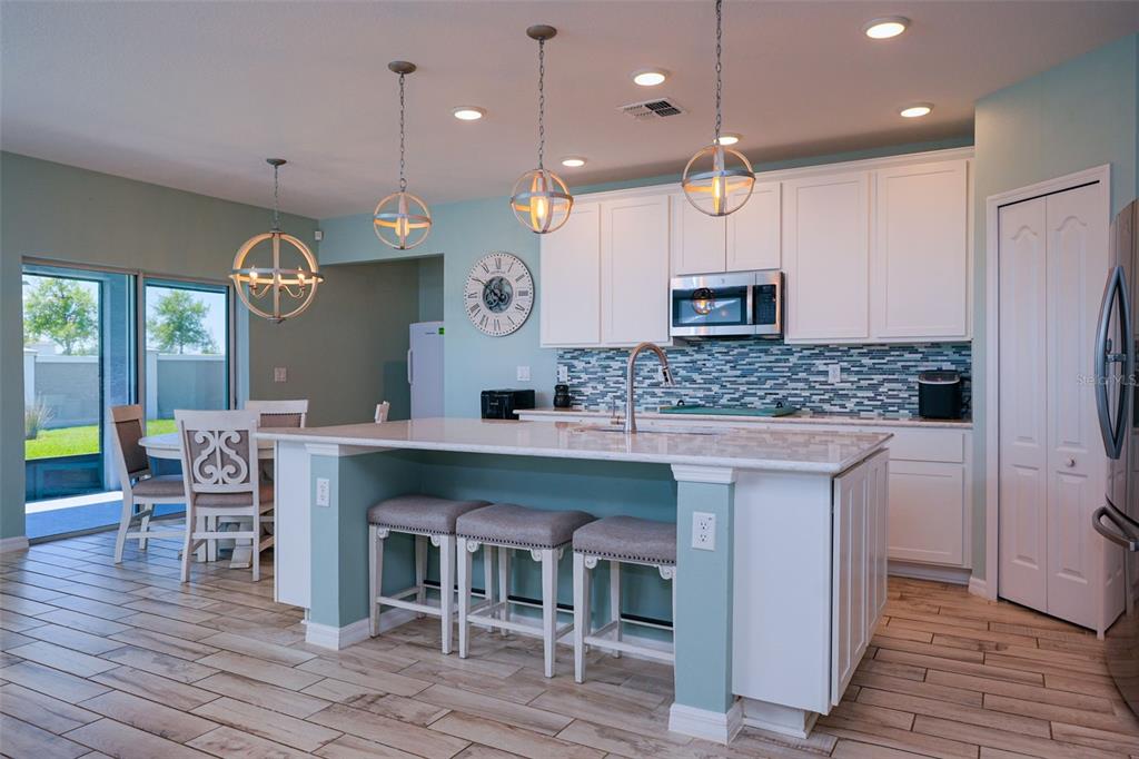 A kitchen with a teal island, white cabinets, light countertops, and wood-look tile flooring — 31300 KALE BROOKS COURT, SAN ANTONIO, FL