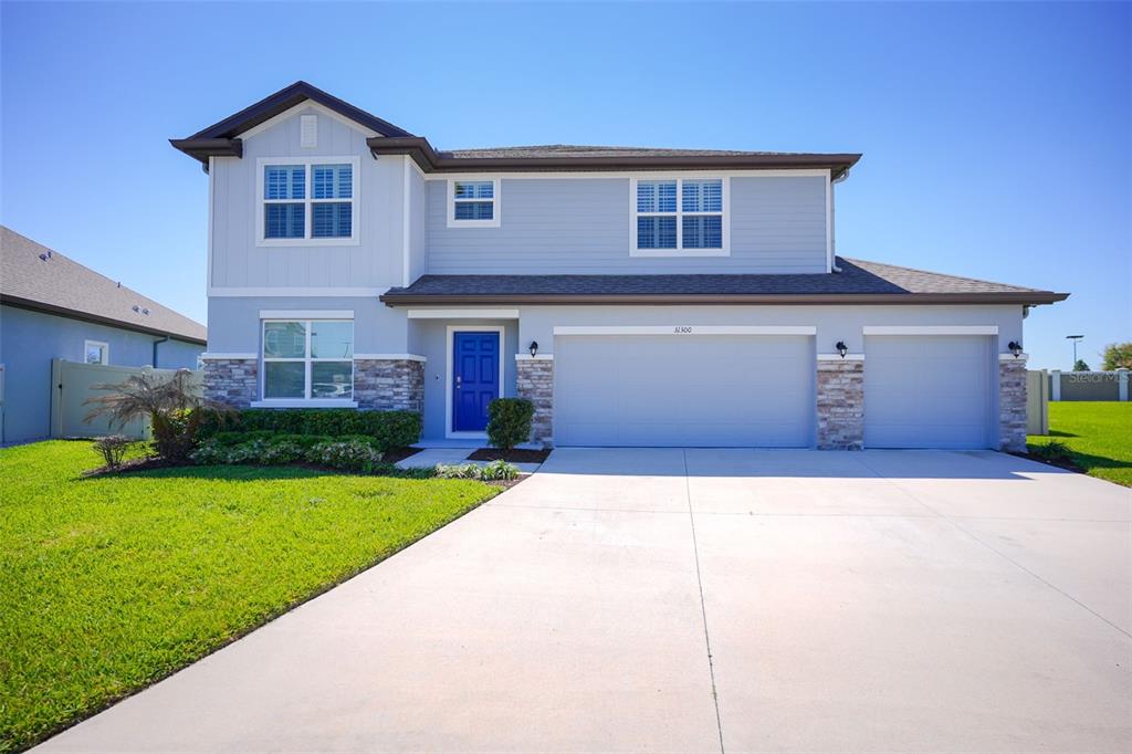 A two-story suburban house with light blue siding, a blue front door, and a three-car garage — 31300 KALE BROOKS COURT, SAN ANTONIO, FL