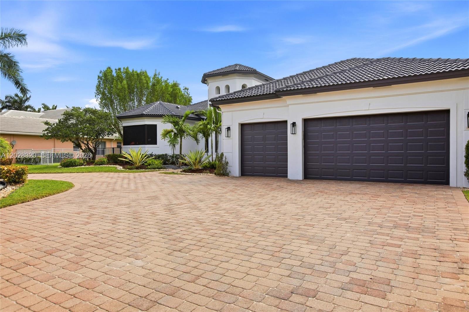 A paved driveway leads to the three-car garage of a white house with a tiled roof — 3250 W Stonebrook Cir, Davie FL 33330, DAVIE, FL