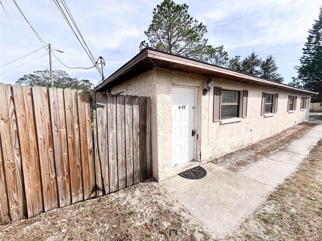 A single-story building exterior features a white door, a wooden fence, and a concrete walkway — 5723 SILVER SPUR DRIVE, HOLIDAY, FL