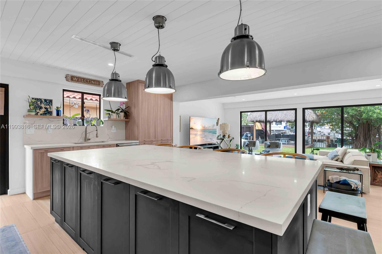 A kitchen with a large white island, dark cabinets, and pendant lights overlooks a patio — 2025 Arch Creek Dr, North Miami FL 33181, NORTH MIAMI, FL