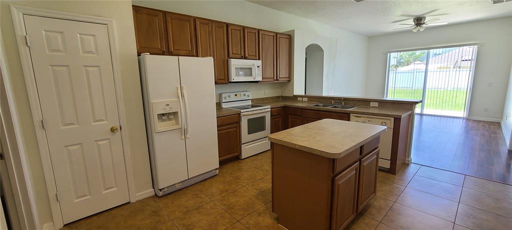 A kitchen features wood cabinets, white appliances, a center island, and tile flooring — 3109 TURNBERRY BOULEVARD, KISSIMMEE, FL