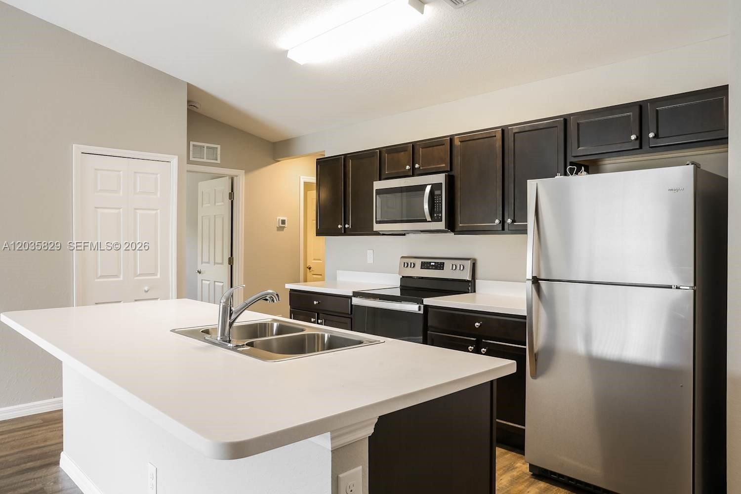 A kitchen features dark wood cabinets, stainless steel appliances, and a white-topped center island — PORT ST. LUCIE, FL