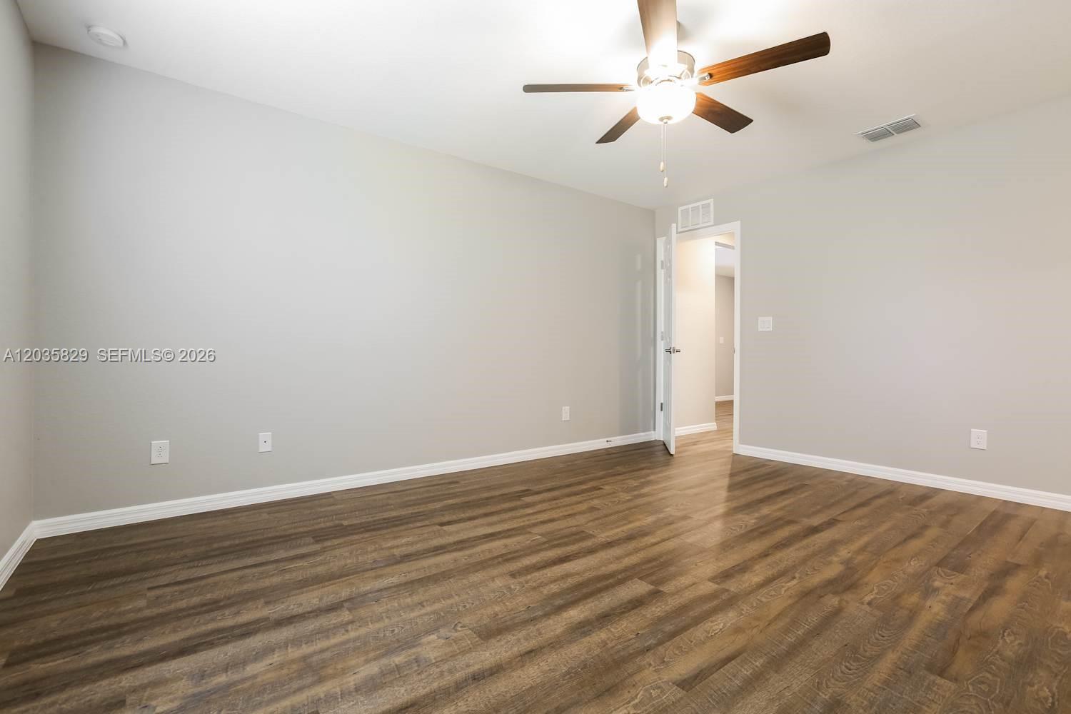 An empty room features light gray walls, dark wood-look flooring, and a ceiling fan — PORT ST. LUCIE, FL