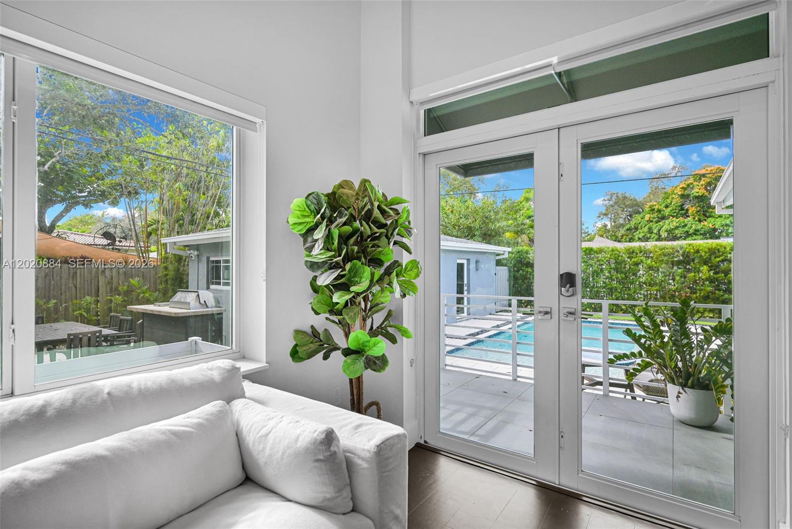 A living room with a white sofa, a potted plant, and glass doors overlooking a pool — 150 NE 50th Ter, Miami FL 33137, MIAMI, FL