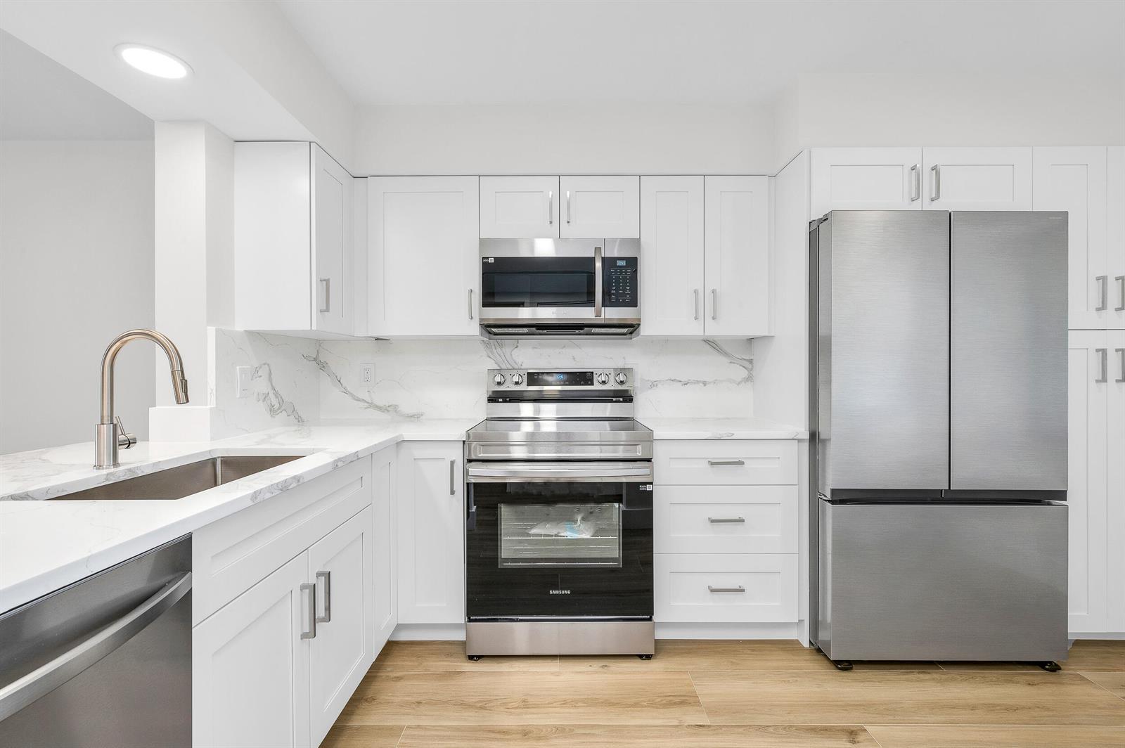A modern kitchen features white cabinets, stainless steel appliances, and marble-patterned countertops and backsplash — 7290 Kinghurst Drive # 301, Delray Beach FL 33446, DELRAY BEACH, FL