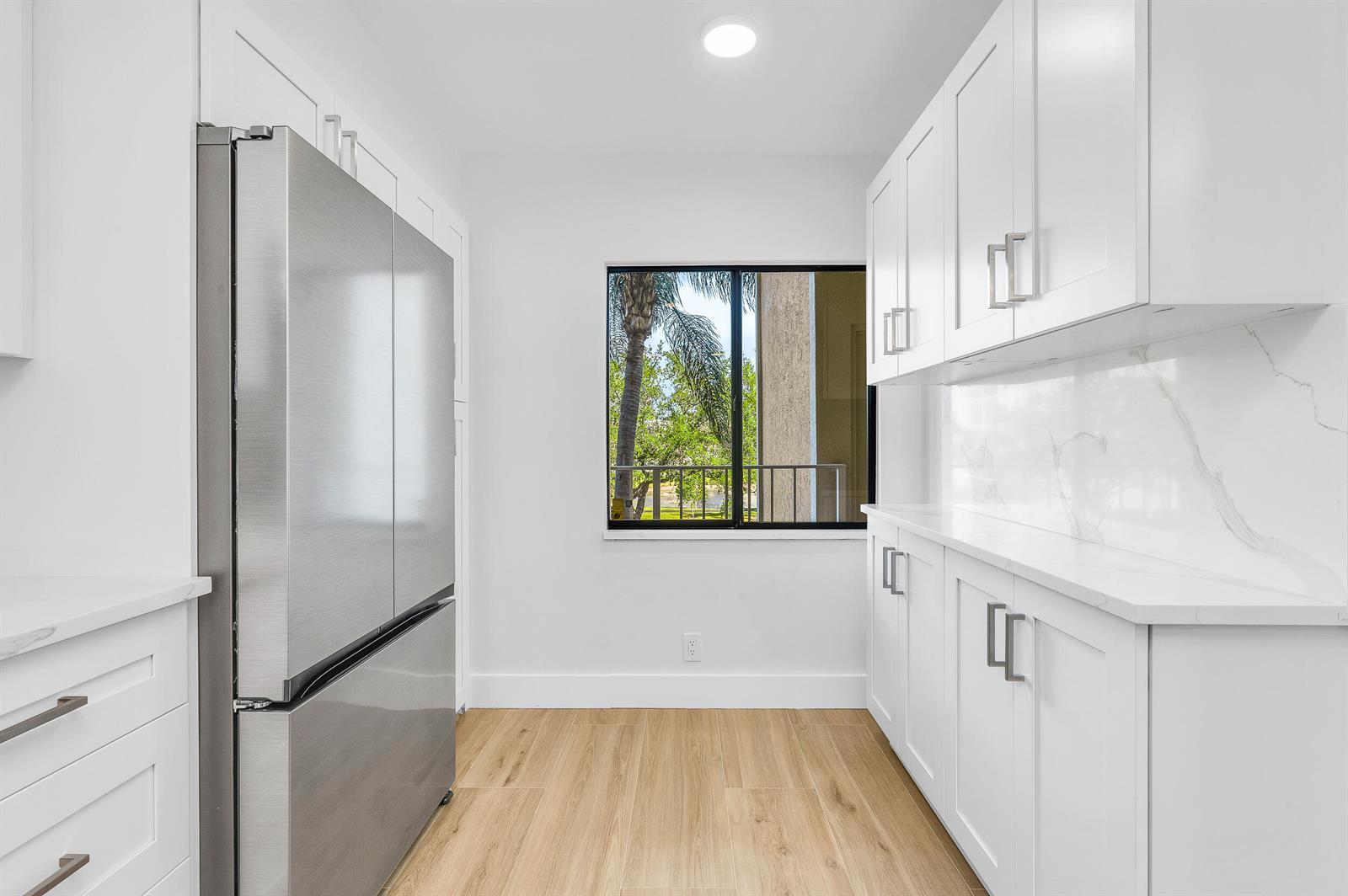 A modern kitchen features white cabinetry, stainless steel appliances, marble-look countertops, and wood-look flooring — 7290 Kinghurst Drive # 301, Delray Beach FL 33446, DELRAY BEACH, FL