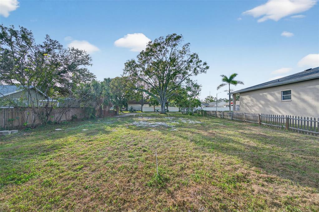 A grassy, vacant residential lot is enclosed by a wooden fence under a blue sky — 6311 HOBSON STREET NE, ST PETERSBURG, FL