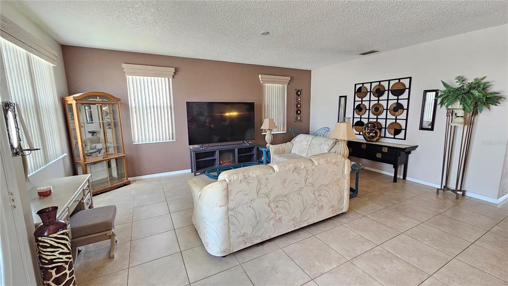 A living room with tile flooring, a floral sofa, a television, and a display cabinet — 543 TERRANOVA CIRCLE, WINTER HAVEN, FL