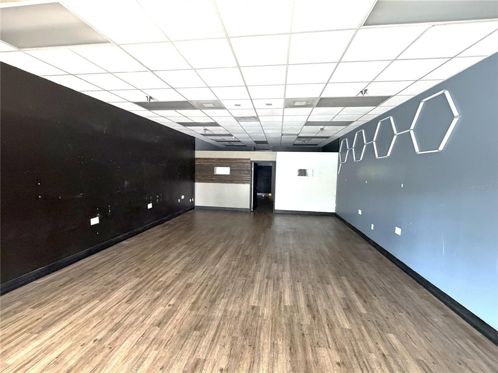 An empty commercial space features wood-look flooring, a drop ceiling, and contrasting black and gray walls — 226 ST. JOE PLAZA DRIVE, PALM COAST, FL