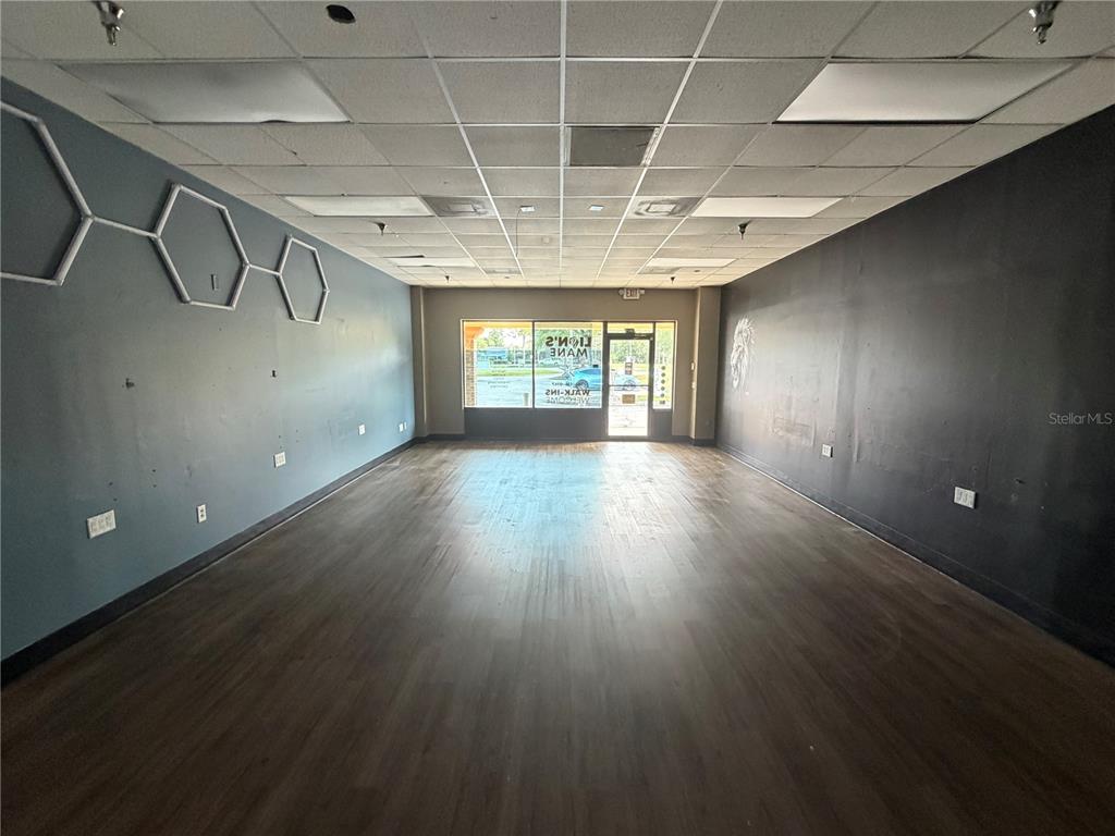 An empty commercial space features dark wood-look flooring, a drop ceiling, and contrasting gray and black walls — 226 ST. JOE PLAZA DRIVE, PALM COAST, FL