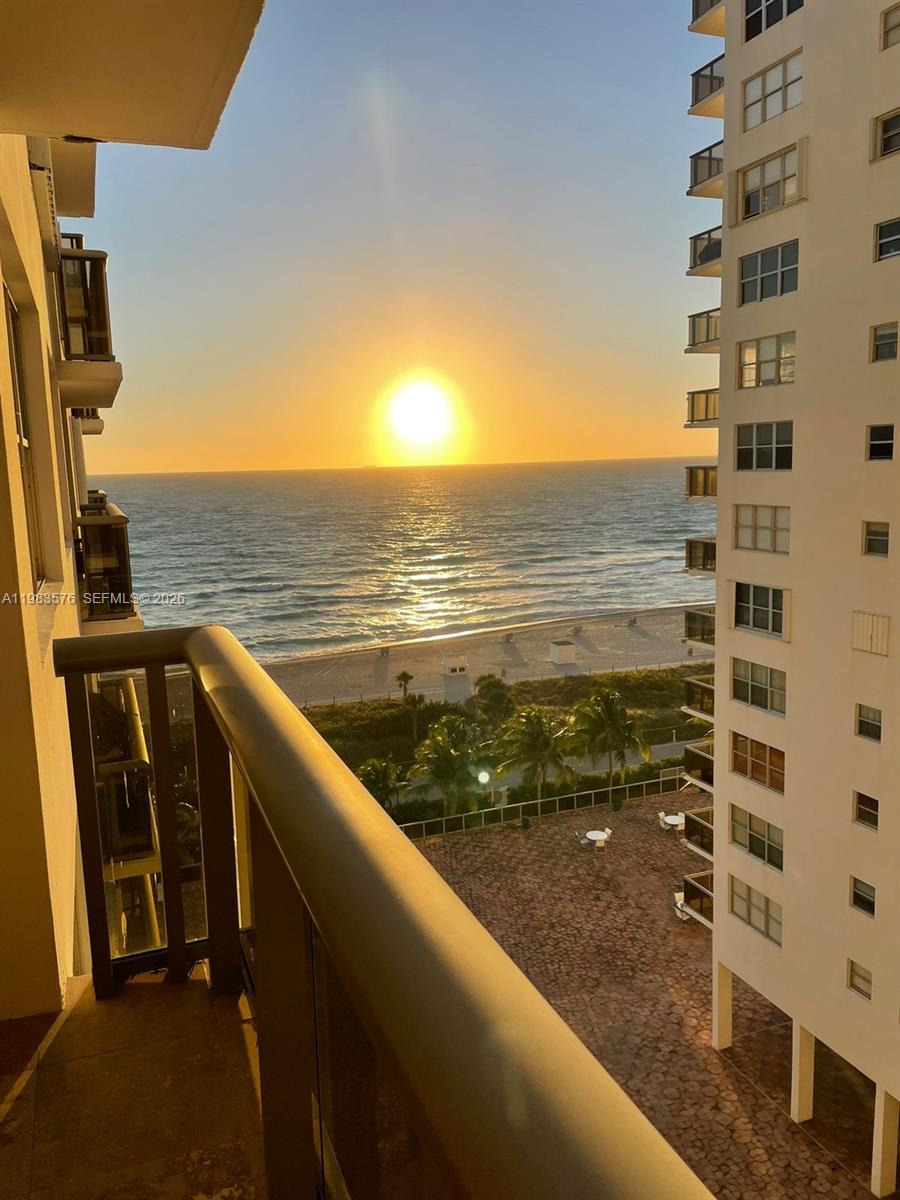 A balcony view overlooks a sandy beach and ocean at sunset next to a high-rise building — 6039 Collins Ave # 1006, Miami Beach FL 33140, MIAMI BEACH, FL