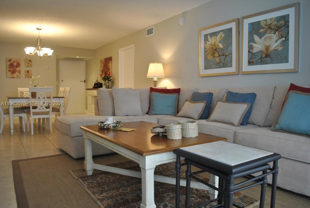 A living room features a large beige sectional sofa, a wooden coffee table, and artwork — 6039 Collins Ave # 1006, Miami Beach FL 33140, MIAMI BEACH, FL