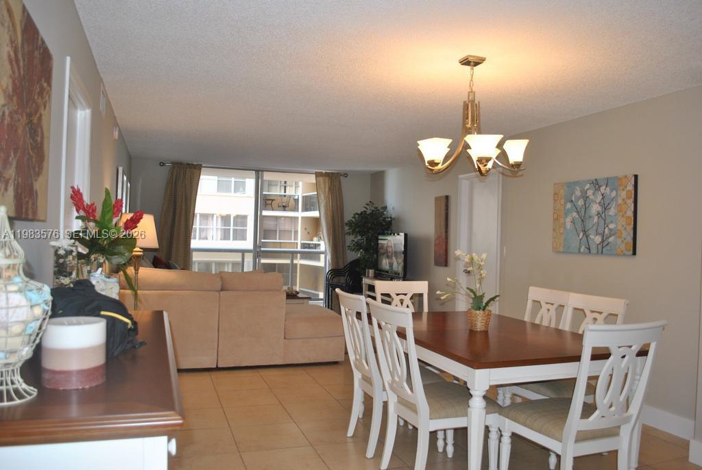 A dining area with a wooden table and white chairs sits adjacent to a living room — 6039 Collins Ave # 1006, Miami Beach FL 33140, MIAMI BEACH, FL