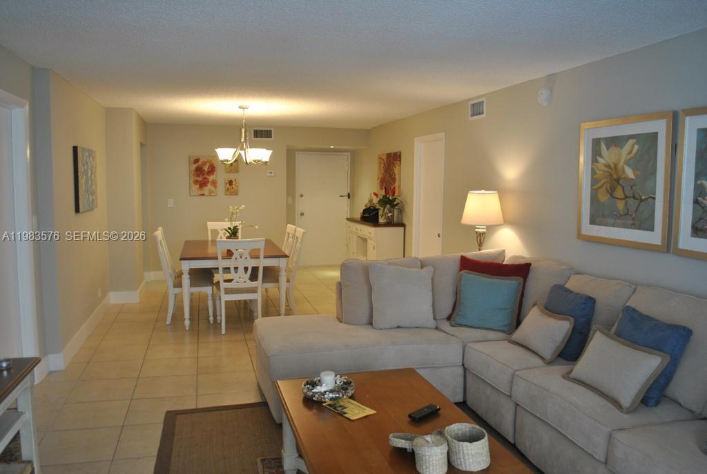 An open-concept living and dining area features tile flooring, a sectional sofa, and neutral walls — 6039 Collins Ave # 1006, Miami Beach FL 33140, MIAMI BEACH, FL