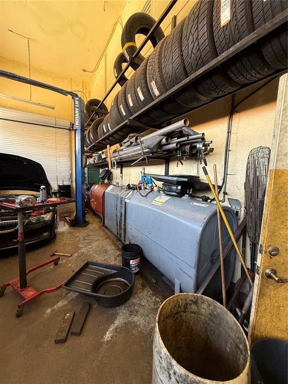 A cluttered auto repair shop features a car lift, stacked tires, and a large metal tank — 23371 HARBORVIEW ROAD UNIT A, PUNTA GORDA, FL