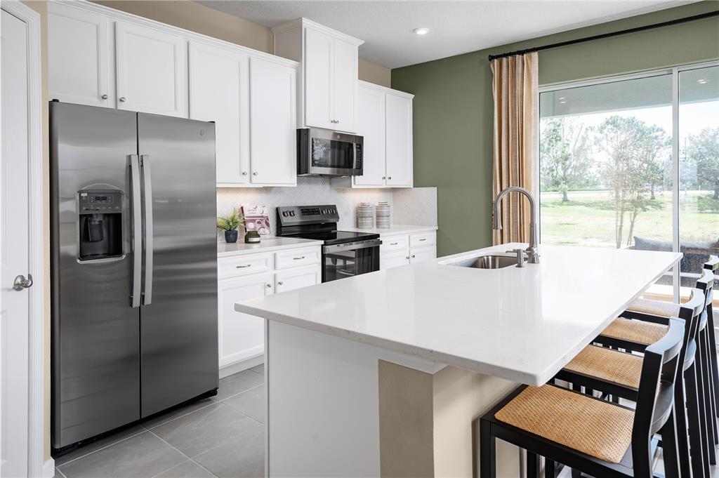 A kitchen features white cabinets, stainless steel appliances, a quartz island, and a sliding door — 12542 AMBER CREEK CIRCLE, LAKEWOOD RANCH, FL