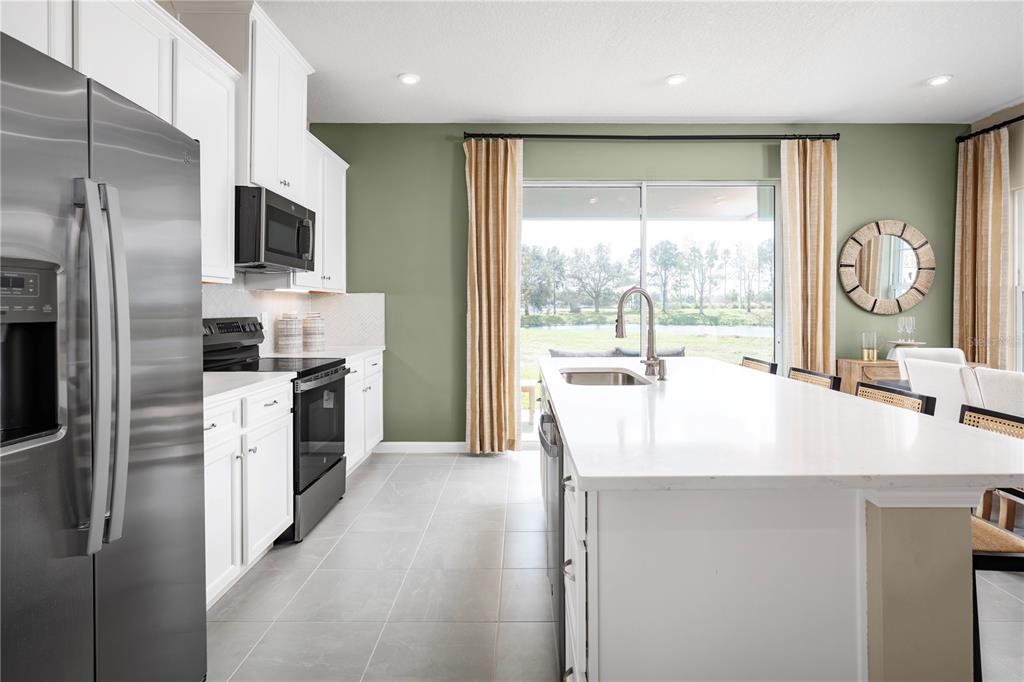 A kitchen with white cabinets, a large island, and a sliding door overlooking a pond — 12542 AMBER CREEK CIRCLE, LAKEWOOD RANCH, FL