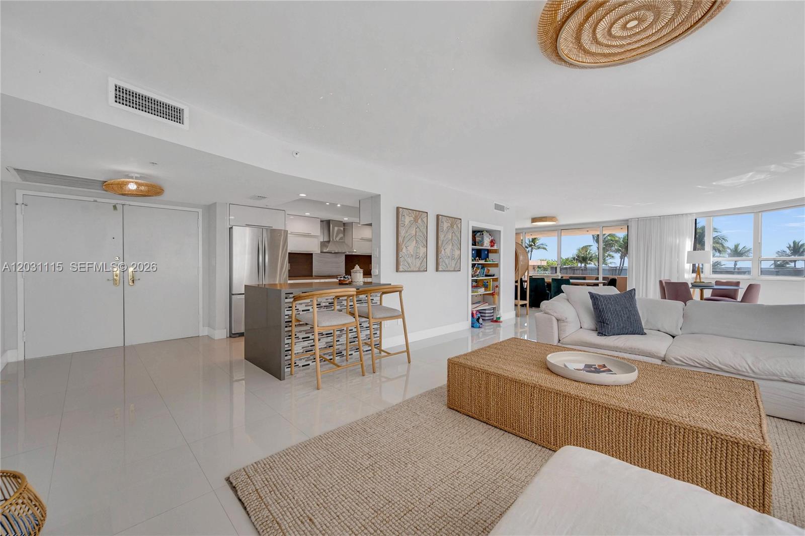 A bright living room features white tile floors, a kitchen island, and a woven coffee table — 10175 Collins Ave # 102, Bal Harbour FL 33154, BAL HARBOUR, FL