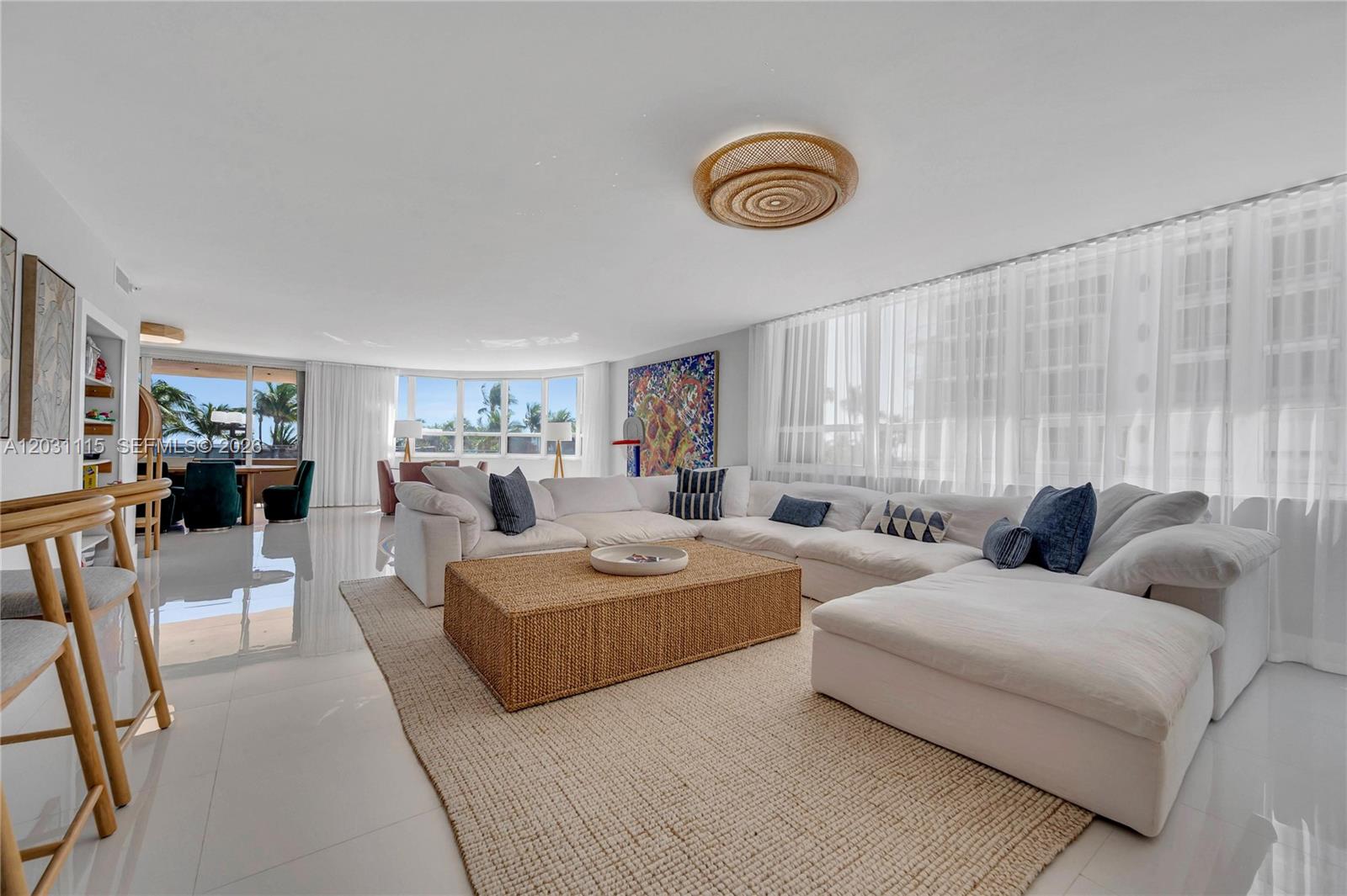 A bright living room features a large white sectional sofa, woven coffee table, and floor-to-ceiling curtains — 10175 Collins Ave # 102, Bal Harbour FL 33154, BAL HARBOUR, FL