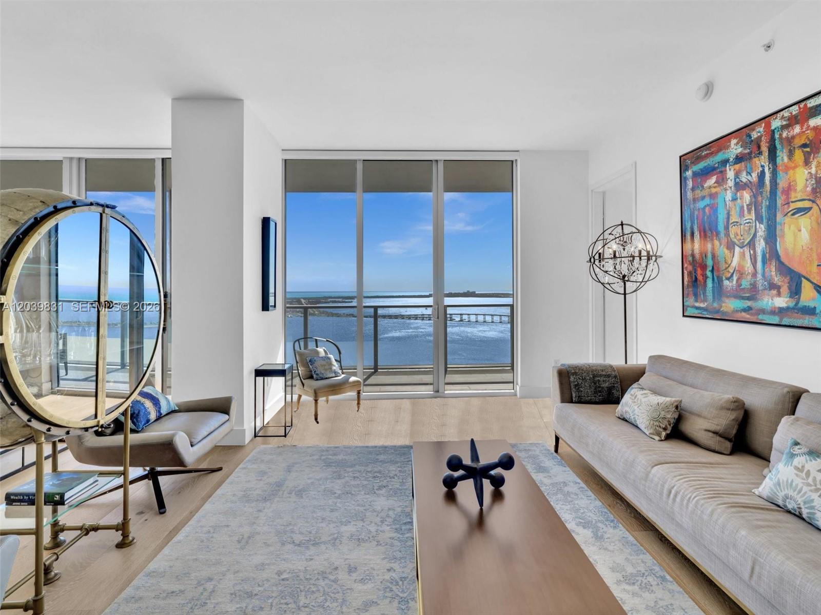 A modern living room features a large window with water views, a sofa, and artwork — 1300 E Brickell Bay Dr # 4202, Miami FL 33131, MIAMI, FL