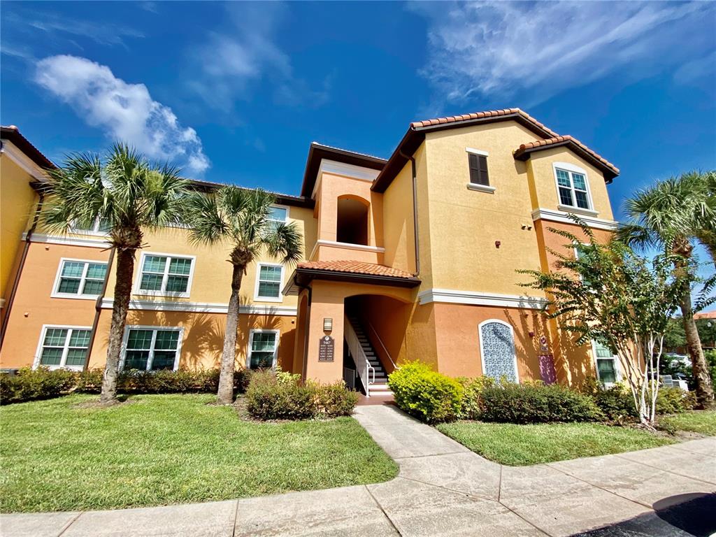 A three-story yellow apartment building with palm trees and a sidewalk in the foreground — 5467 VINELAND ROAD UNIT 6301, ORLANDO, FL